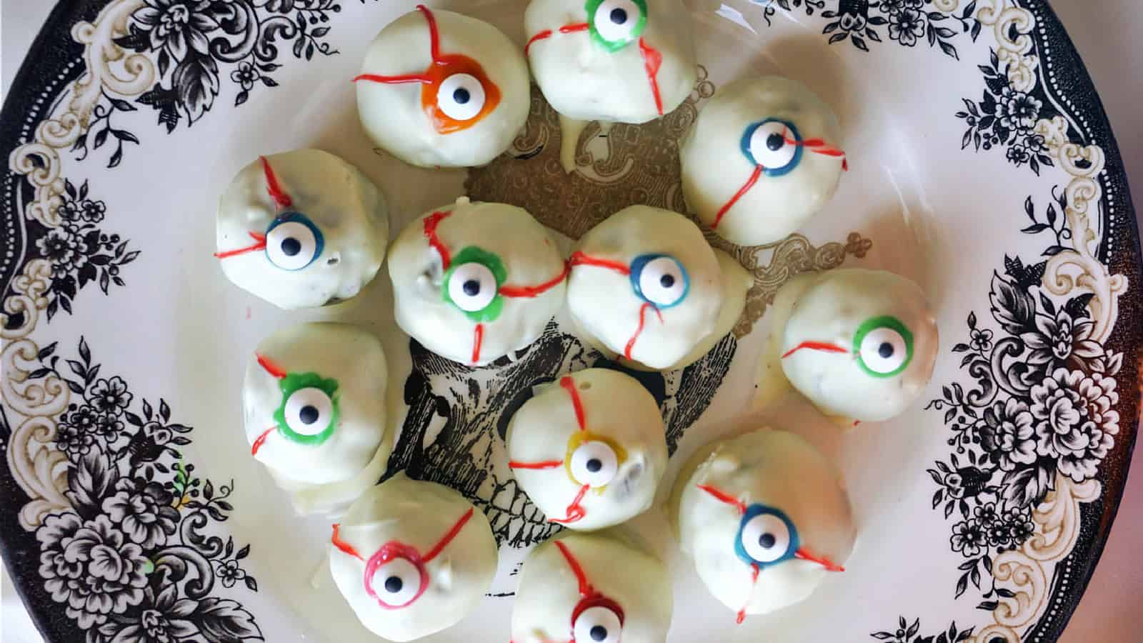A plate of white chocolate truffles decorated to look like eyeballs with colorful candy irises and red icing veins, placed on a black and white patterned plate.