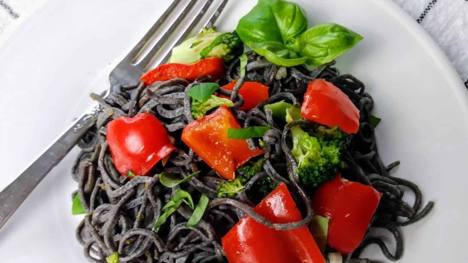 black soybean spaghetti with broccoli and red peppers and fresh basil and fork on plate.