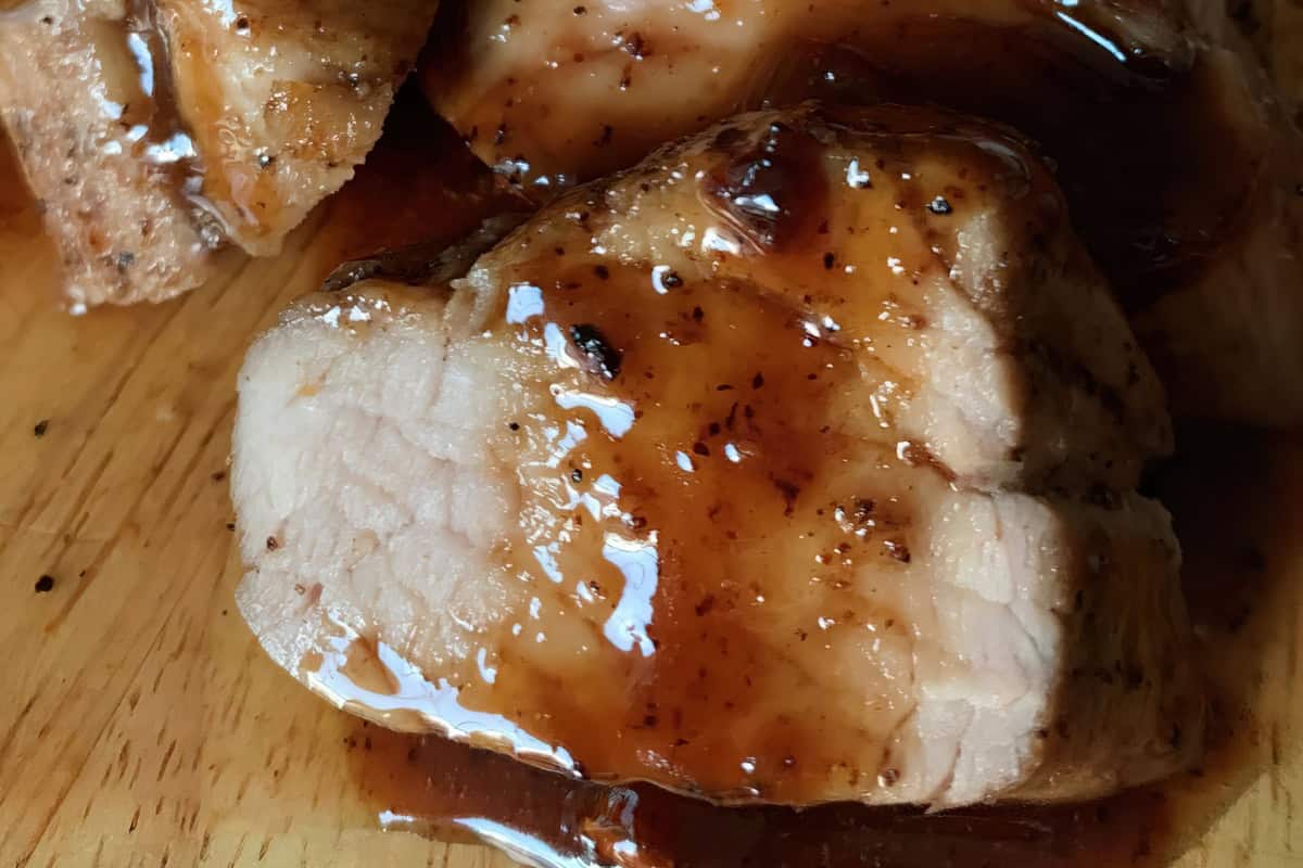 Close-up of glazed pork medallions on a wooden surface. The meat is coated in a shiny sauce, highlighting its juicy texture and appetizing appearance.