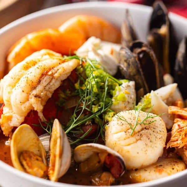 A bowl of seafood stew with shrimp, scallops, clams, mussels, and fish pieces, topped with fresh green herbs.