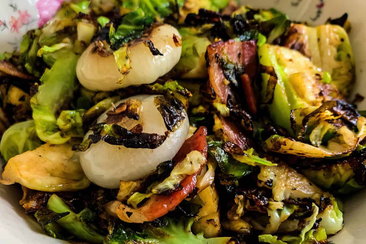 A close-up of a bowl containing grilled onions, bell peppers, and charred greens.