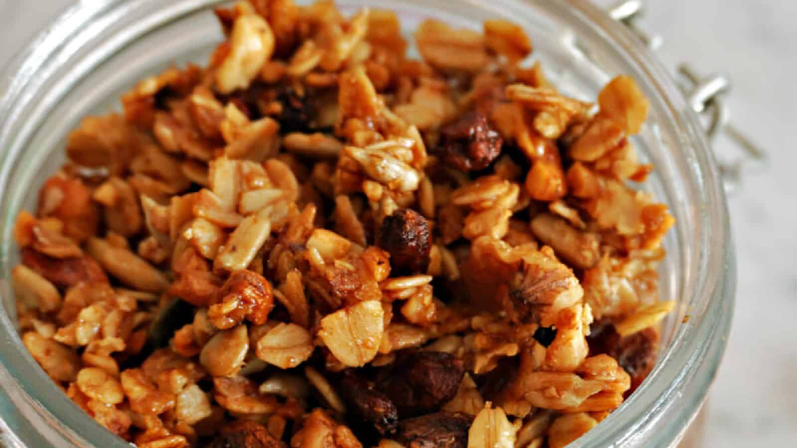 A jar filled with homemade granola, featuring oats, nuts, and seeds, creating a crunchy golden-brown texture.