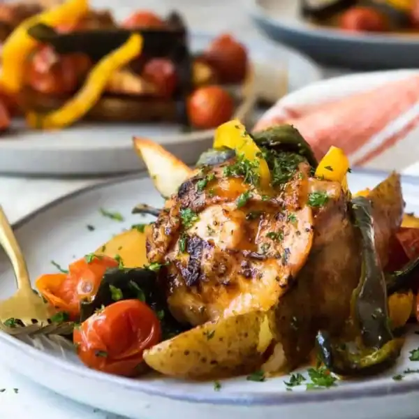 Roasted chicken with potatoes, cherry tomatoes, and sliced bell peppers, garnished with chopped herbs on a gray ceramic plate.