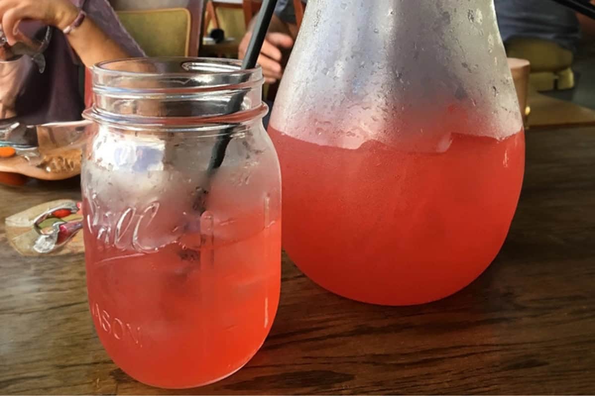 A glass jar and a pitcher filled with pink liquid are on a wooden table.