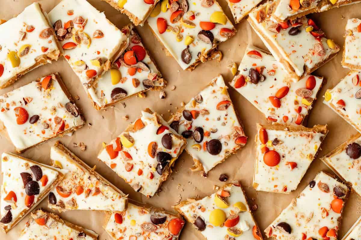 Top view of white chocolate-covered square and triangular bars topped with colorful candy pieces on a parchment paper surface. The bars are scattered in an irregular pattern.