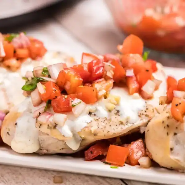 Three chicken breasts with melted cheese and tomato salsa on a white rectangular plate.
