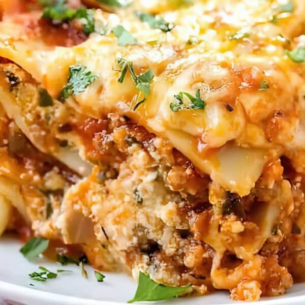 Close-up of lasagna with visible layers of pasta, meat, ricotta cheese, tomato sauce, melted cheese, and chopped parsley on top.