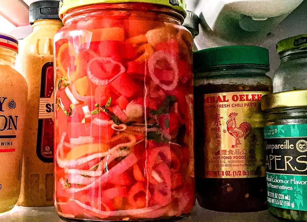 A jar of pickled sweet peppers in a refrigerator. 