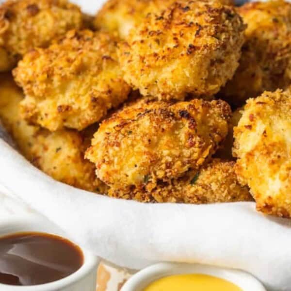 A basket of breaded, baked chicken nuggets beside small containers of barbecue and honey mustard dipping sauces.