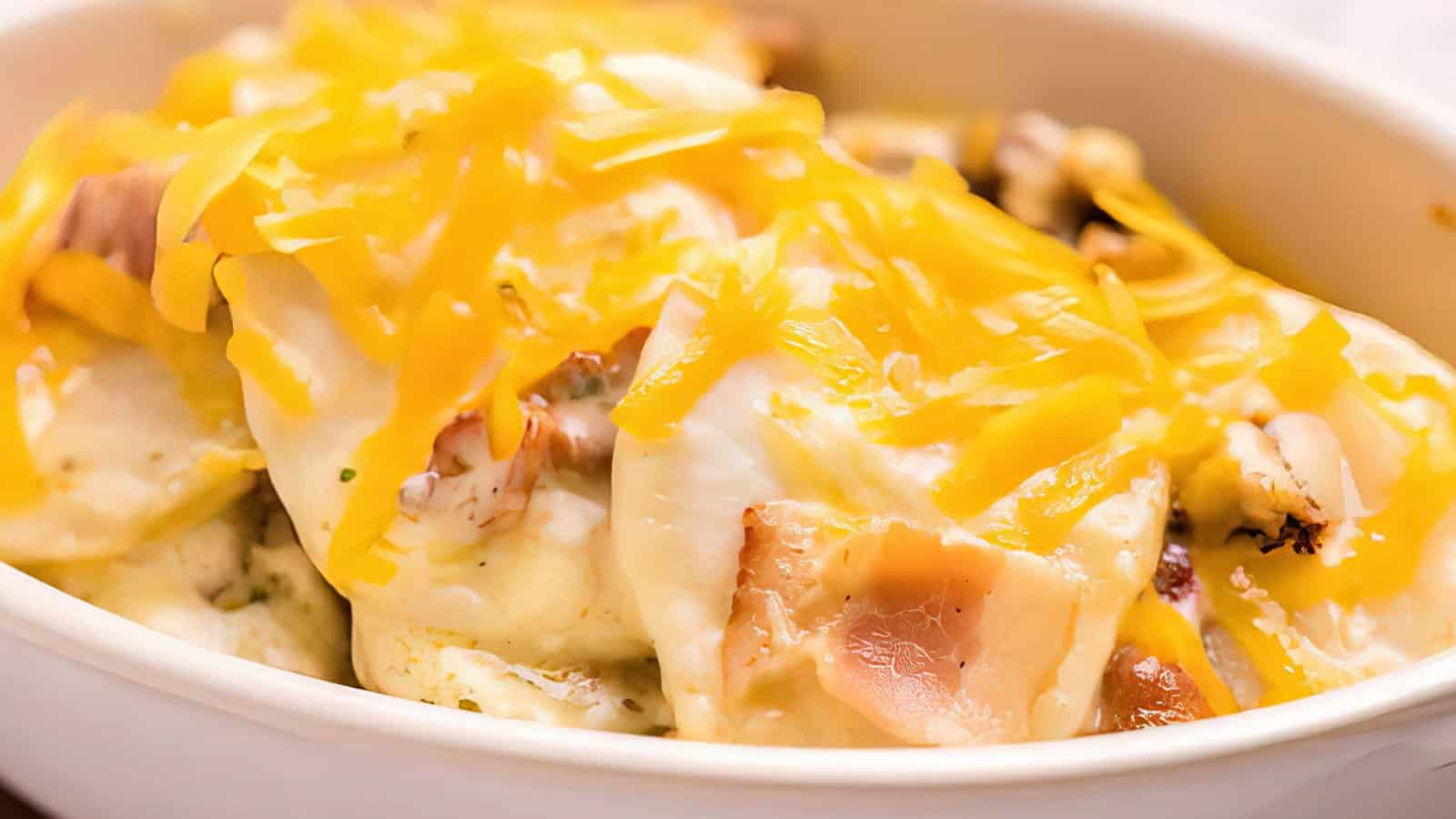 A close-up of a dish featuring baked chicken covered with melted cheddar cheese in a white ceramic dish. The cheese is generously sprinkled on top, giving the dish a rich, gooey texture.