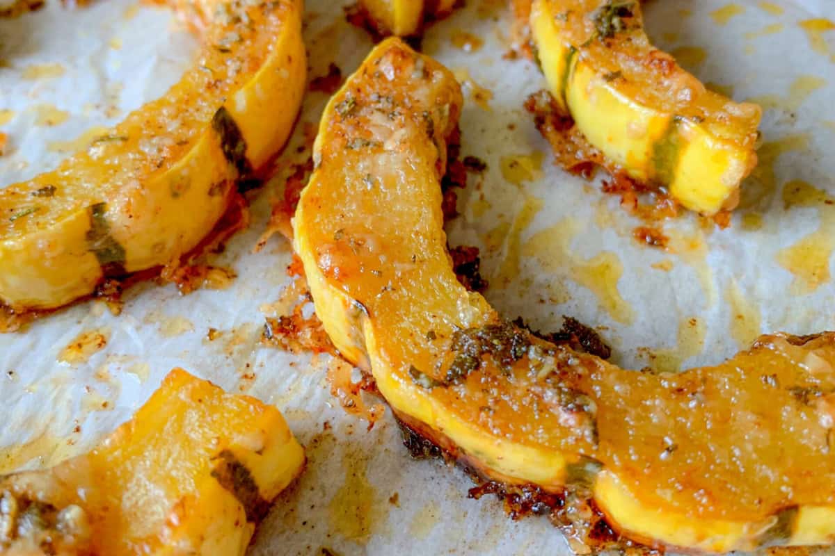 Roasted squash slices on parchment paper, topped with herbs and melted cheese.