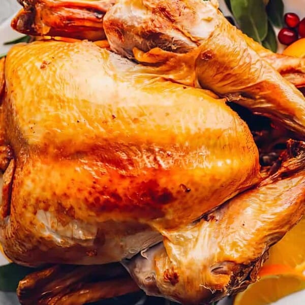 A roasted turkey on a white platter, garnished with orange slices, cranberries, bay leaves, and sprigs of rosemary.