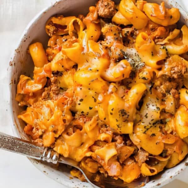 A bowl of cheesy pasta mixed with ground beef and herbs, accompanied by a fork.