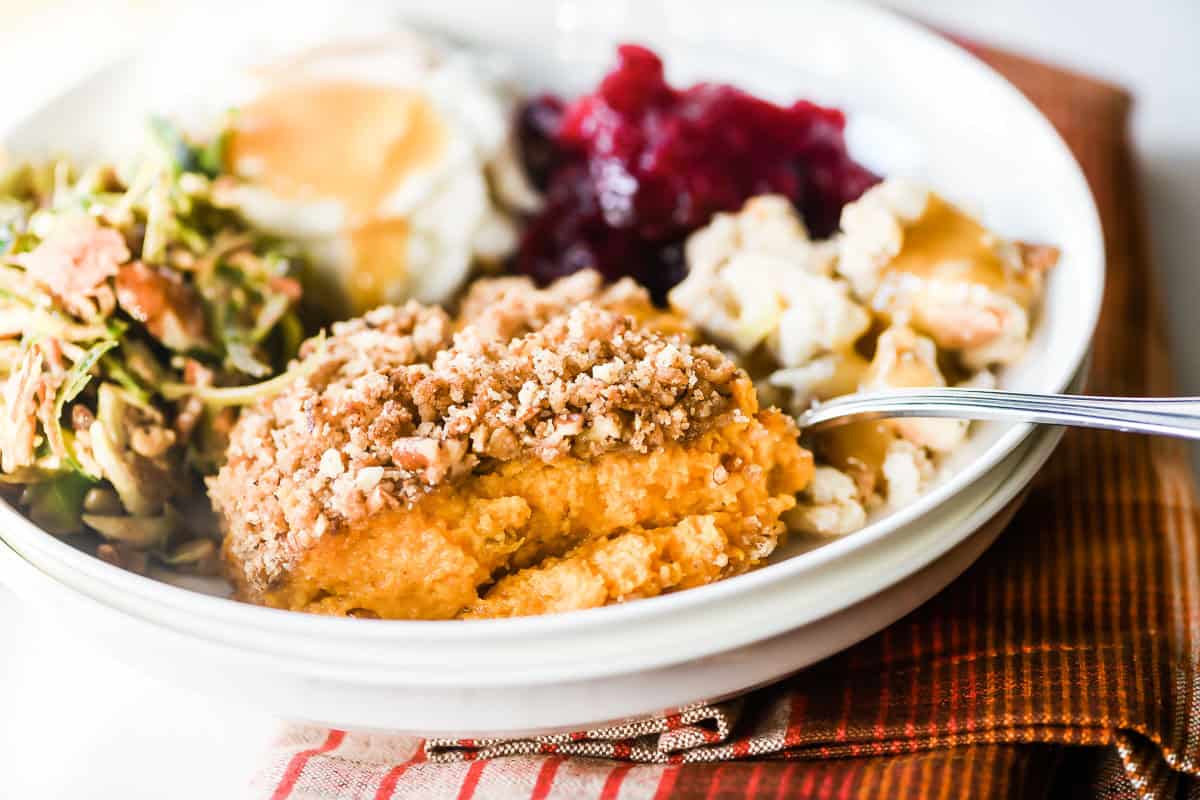 Sweet potato casserole, shredded salad, mashed potatoes with gravy, cranberry sauce, and a poached egg on a plate.
