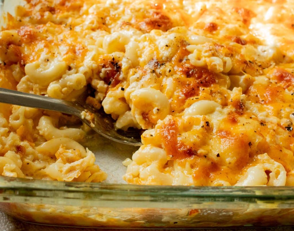 A glass baking dish filled with baked macaroni and cheese, with a spoon scooping out a serving.