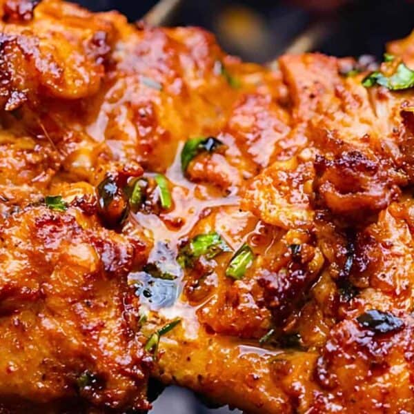 Close-up of grilled marinated chicken with chopped herbs, golden-brown and slightly charred surface, and a juicy texture.