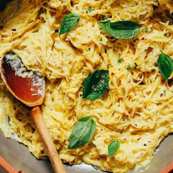 A skillet filled with creamy spaghetti squash topped with fresh basil leaves, with a wooden spoon resting inside.