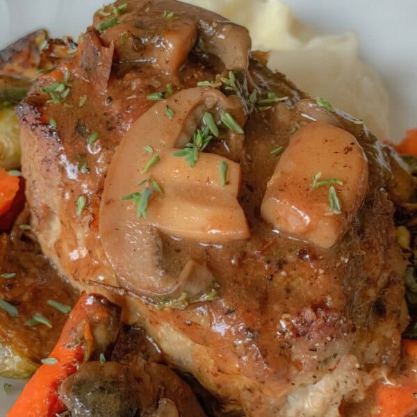 A plate with steak topped with mushroom gravy, alongside roasted carrots, Brussels sprouts, and mashed potatoes.