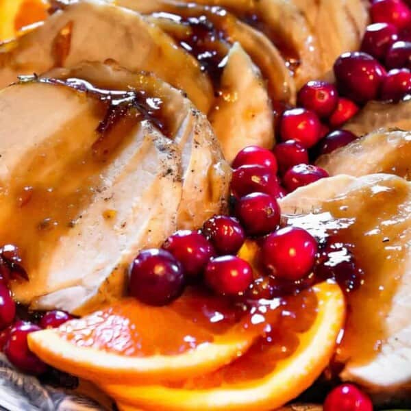 Sliced roast turkey topped with brown gravy, garnished with orange slices, fresh cranberries, and rosemary on a serving platter.