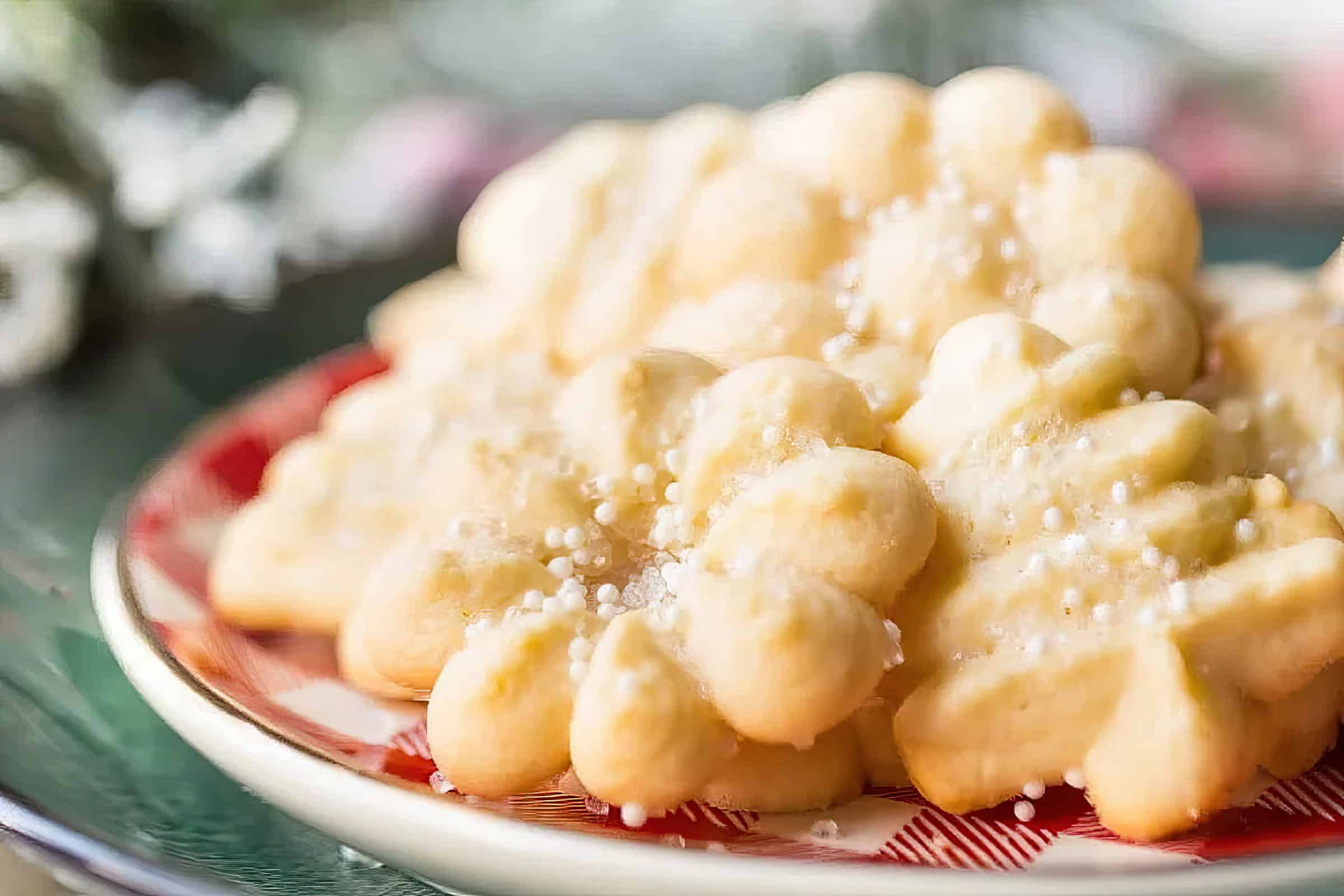 A close-up of star-shaped butter cookies on a red and white checkered plate. The cookies are sprinkled with white sugar crystals, creating a festive and appetizing appearance. The background is softly blurred.