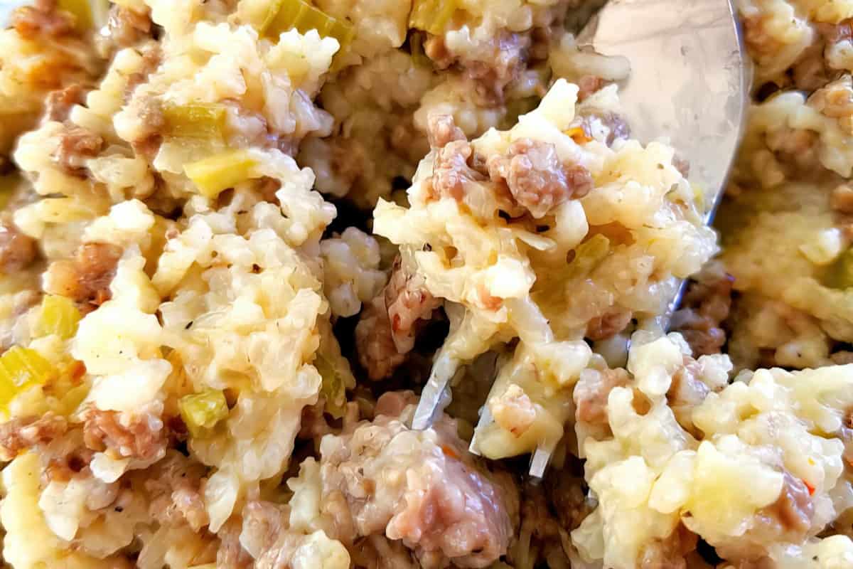 Close-up of a spoon scooping a dish with creamy rice, ground meat, and small pieces of green vegetables. The mixture appears hearty and well-blended.