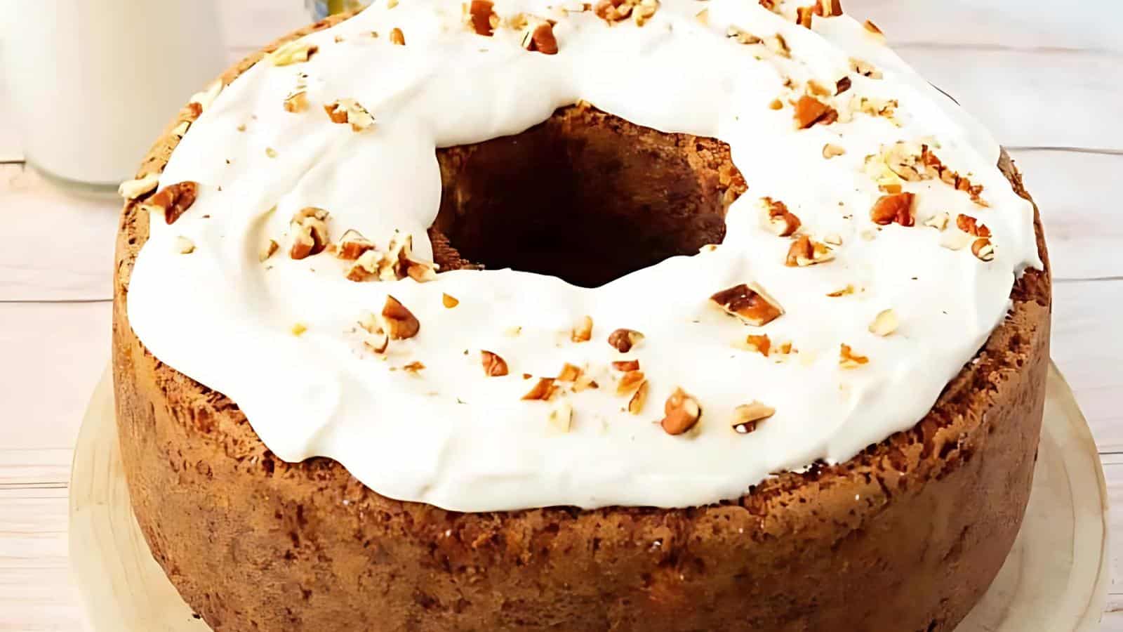 A ring-shaped cake with white frosting, sprinkled with chopped nuts, on a wooden board.