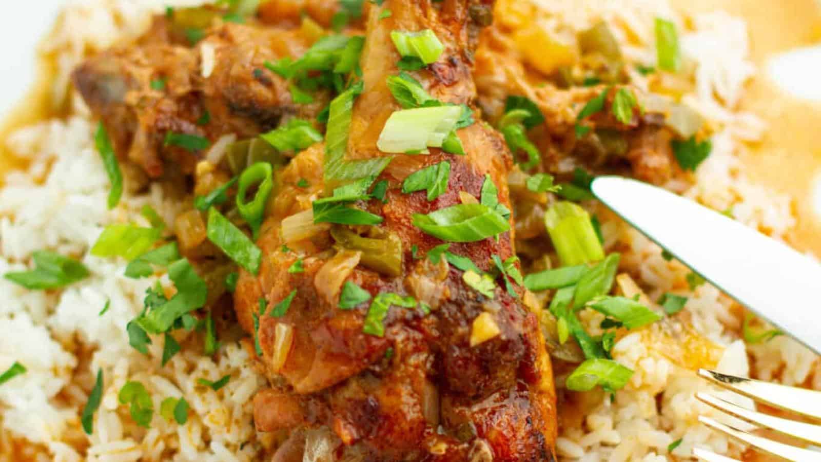 The image shows seasoned, cooked chicken on a bed of rice, garnished with chopped green onions and herbs. A fork and knife are partially visible on the side.