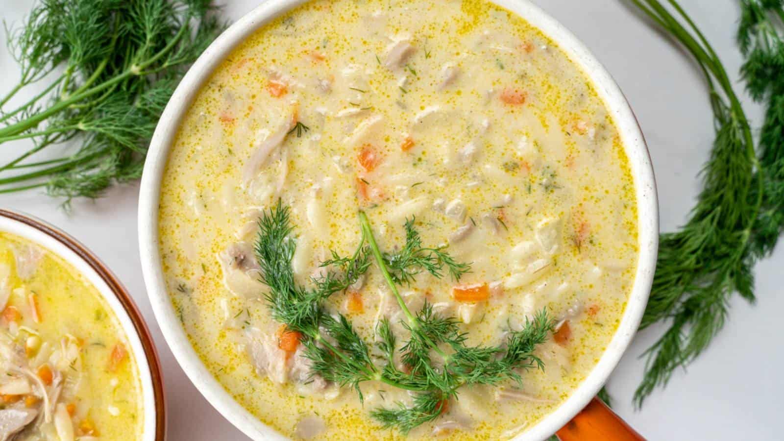 The image shows a bowl of creamy chicken soup containing shredded chicken, carrots, and a garnish of fresh dill, with sprigs of dill placed around the bowl.