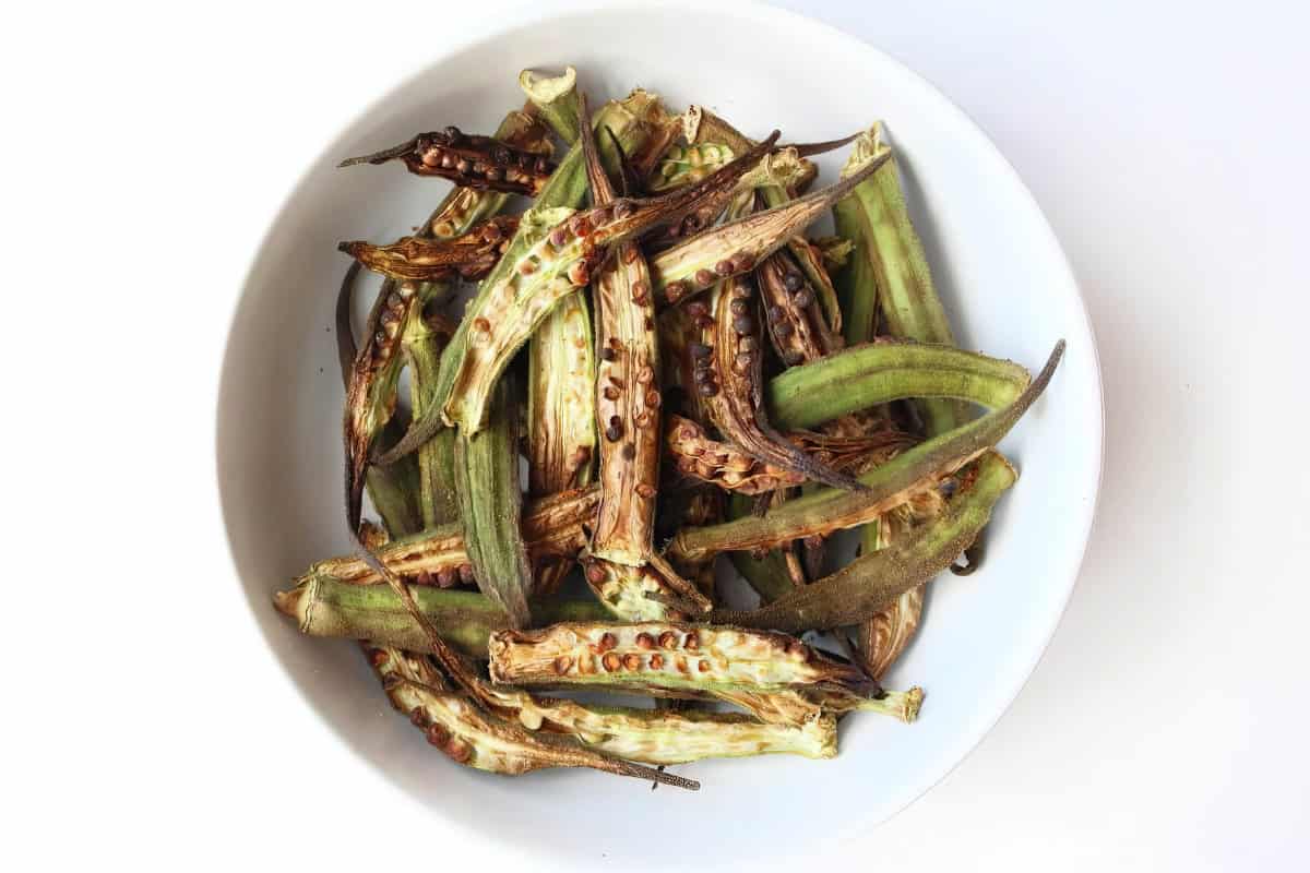 A white bowl containing roasted okra with browned and crispy edges, set against a white background.