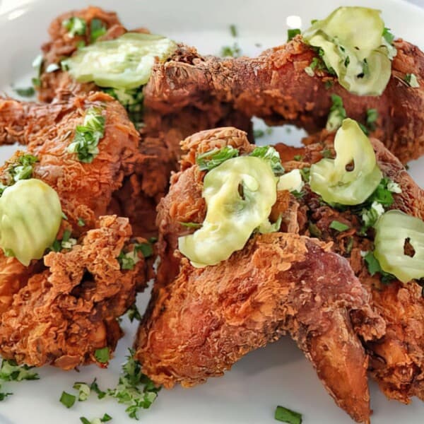 Four Southern fried chicken wings topped with sliced pickles and chopped herbs, served on a white plate.