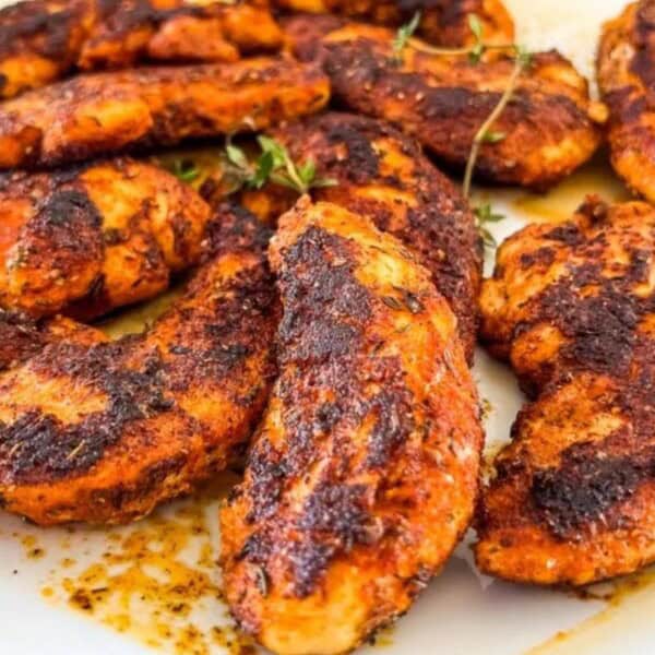 The image shows grilled chicken pieces with a charred surface, garnished with sprigs of herbs.
