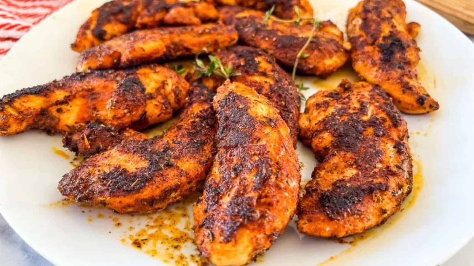 The image shows grilled chicken pieces with a charred surface, garnished with sprigs of herbs.