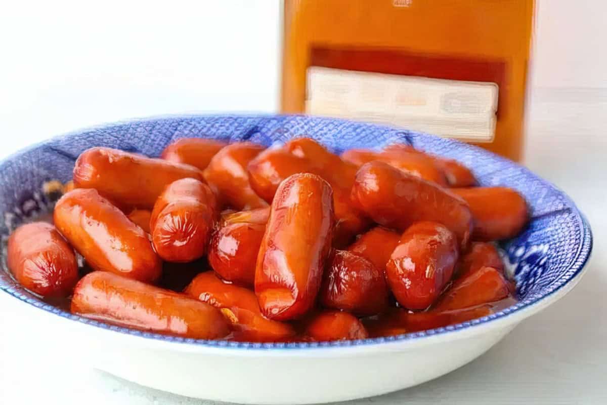 A bowl of cocktail sausages. A partially visible bottle in the background.