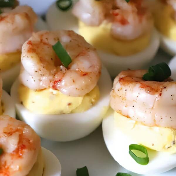 Halved boiled eggs topped with seasoned shrimp and sliced green onions, arranged on a white plate.