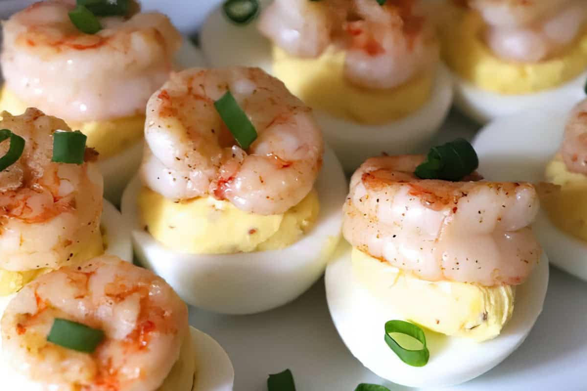 Deviled eggs topped with seasoned shrimp and garnished with sliced green onions. The eggs are arranged on a white plate, showcasing their creamy yolk mixture and the vibrant contrast of the toppings.