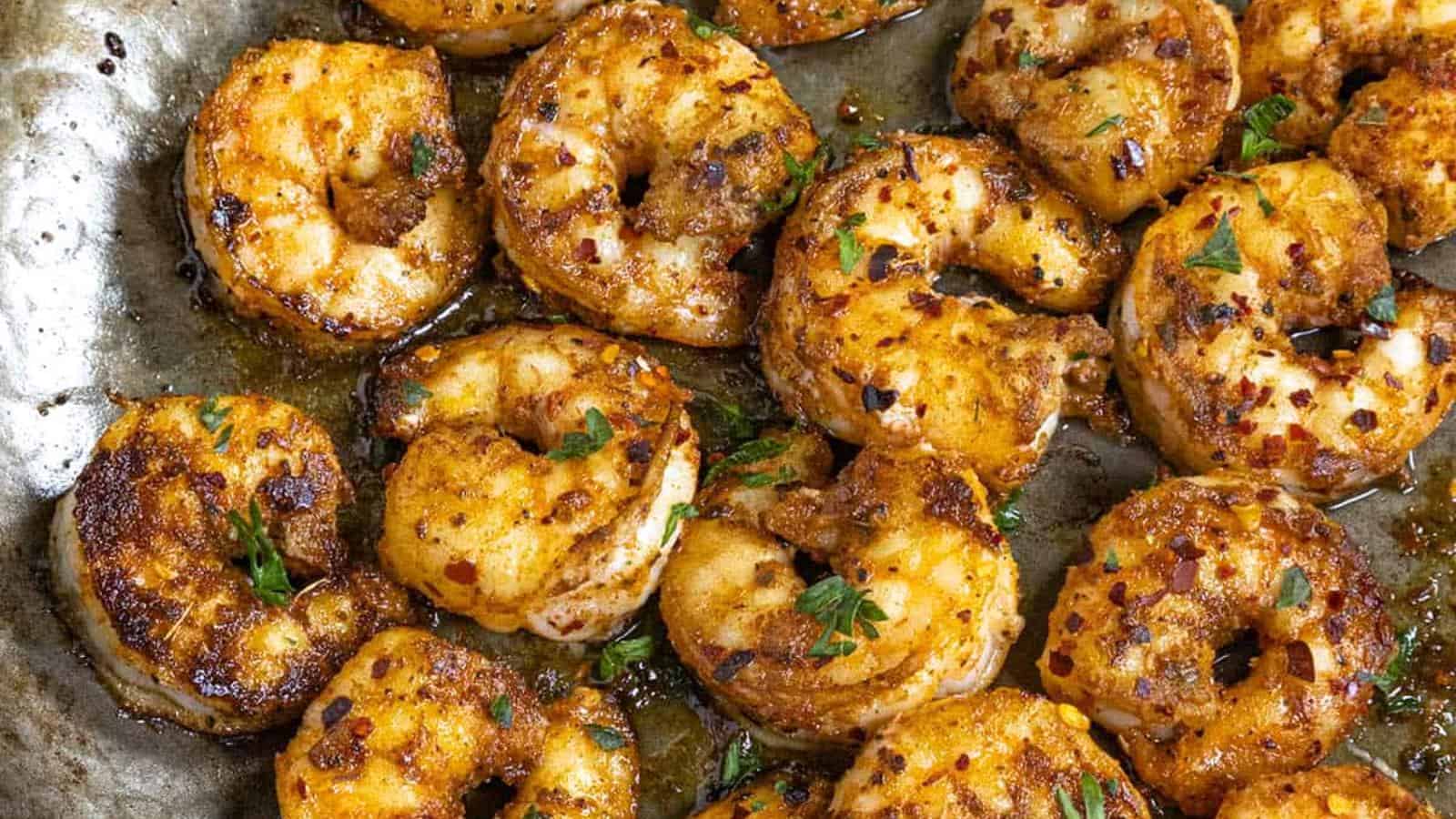 Cooked shrimp on a metal surface with herbs sprinkled on top.