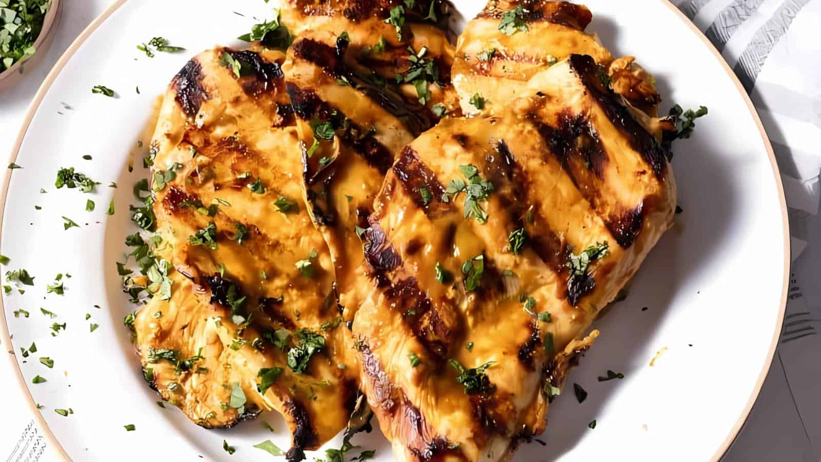 Grilled chicken breasts and chopped herbs on a white plate.