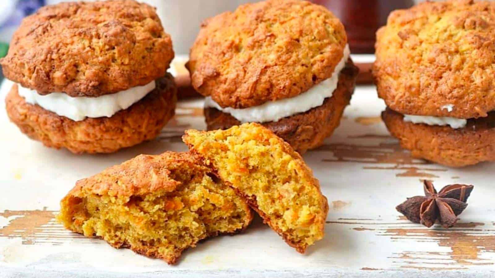 The image shows four carrot cake cookies on a wooden surface, some of which are filled with cream. One of the cookies is broken in half. There is a star anise placed beside them.