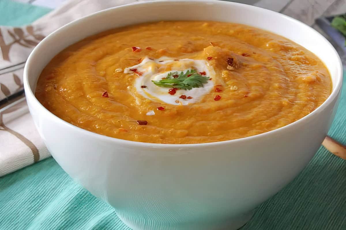 A bowl of pumpkin soup with cream, red pepper flakes, and a cilantro leaf on top.
