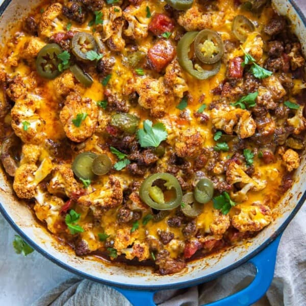 The image shows a skillet with melted cheese, ground meat, cauliflower, sliced jalapeños, and chopped cilantro.
