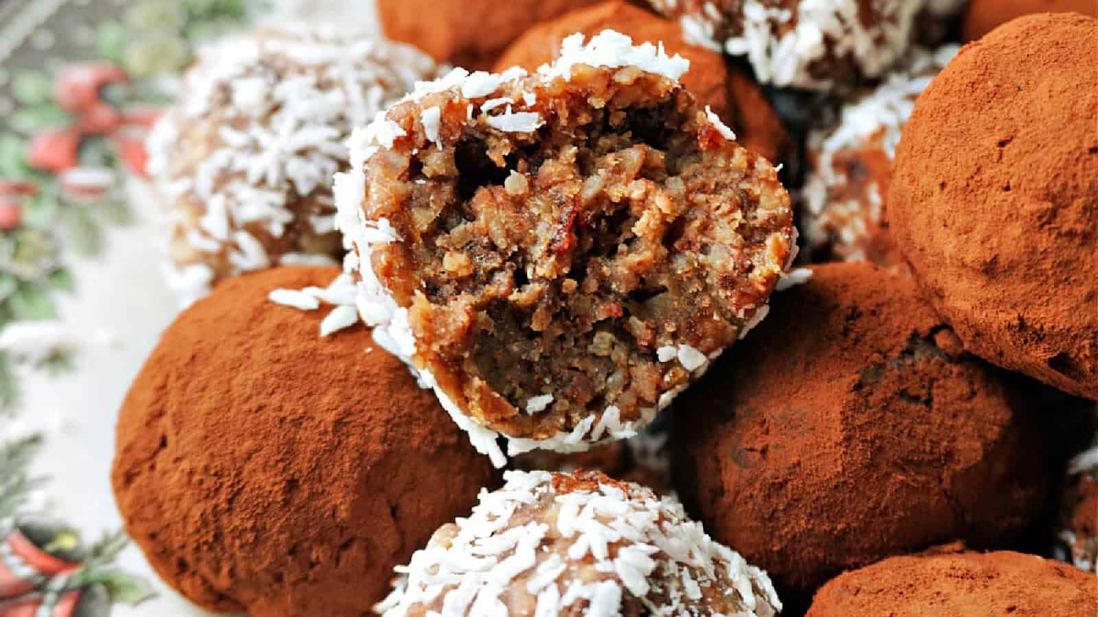 A close-up of truffles coated in cocoa powder and shredded coconut. One truffle is partially eaten, showing a dense, nutty filling.