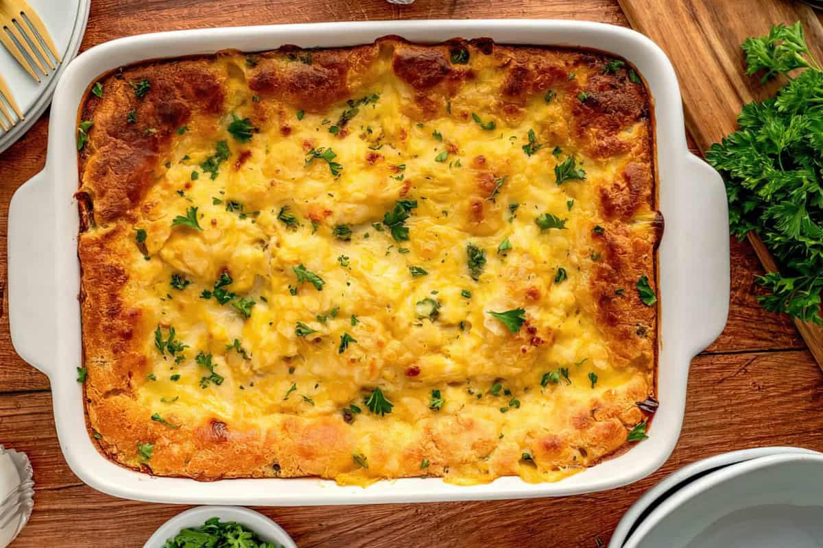 A white dish containing a baked casserole topped with melted cheese and chopped parsley.