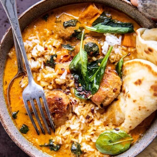 A bowl of curry with rice, spinach, pieces of meat, flatbread on the side, and a fork resting nearby.