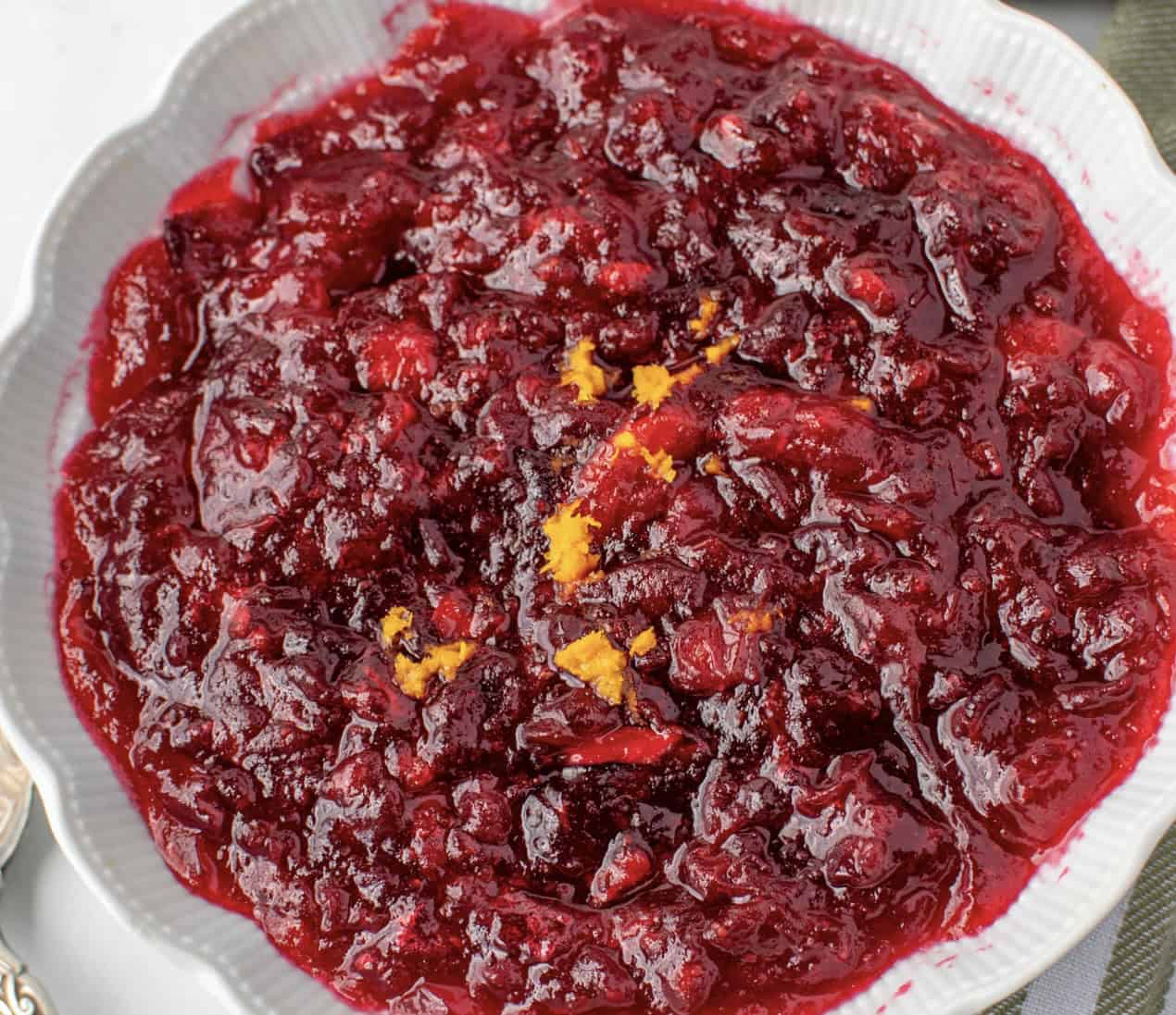 A white bowl containing cranberry sauce with orange zest on top.