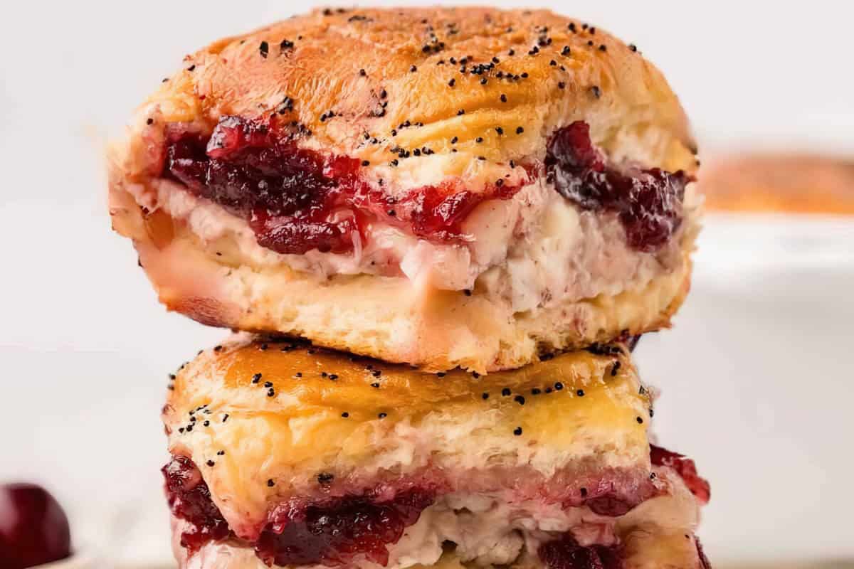 Two stacked sandwiches with poppy seed buns, cream cheese, and cranberry sauce.