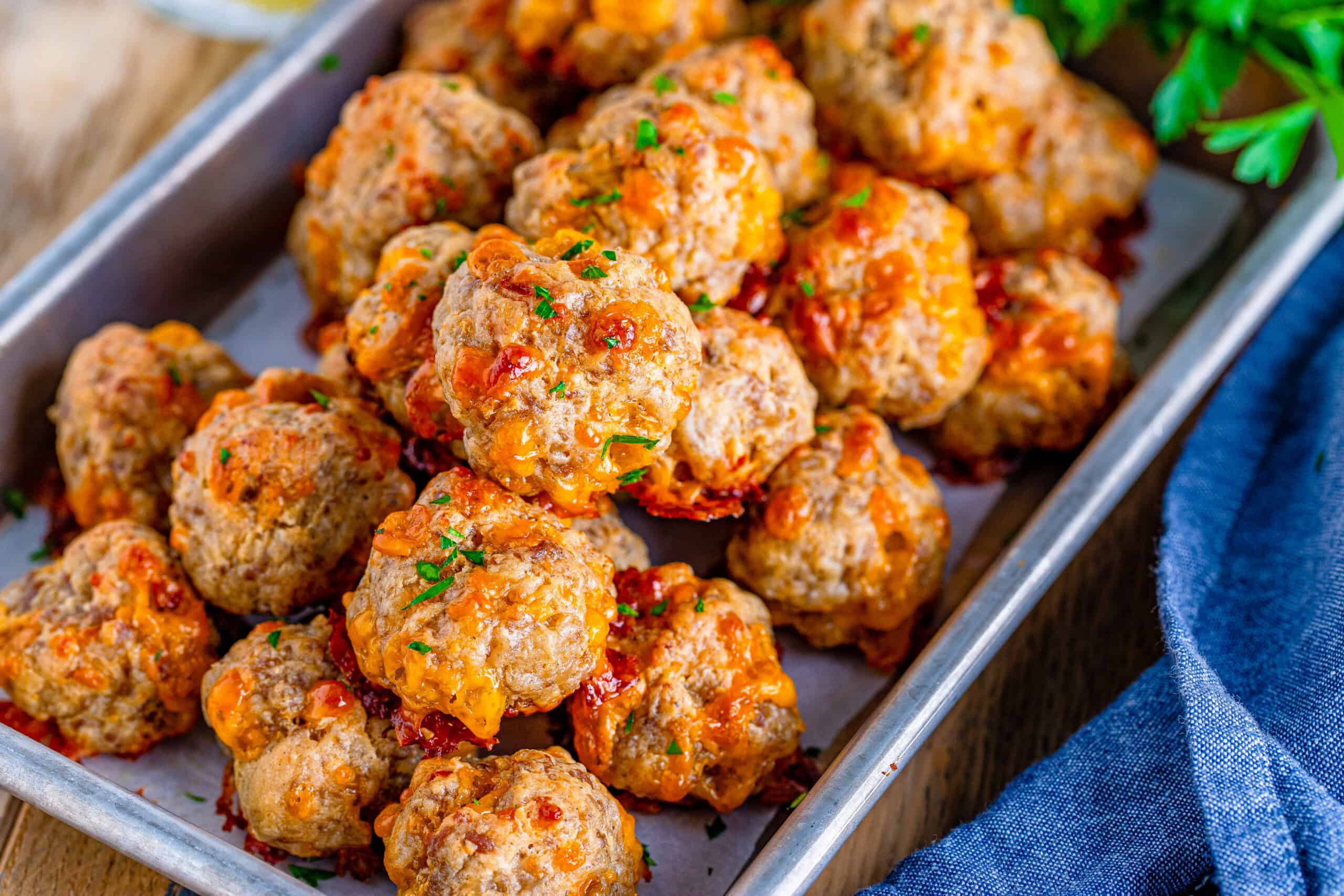 A tray containing browned sausage balls and chopped herbs.