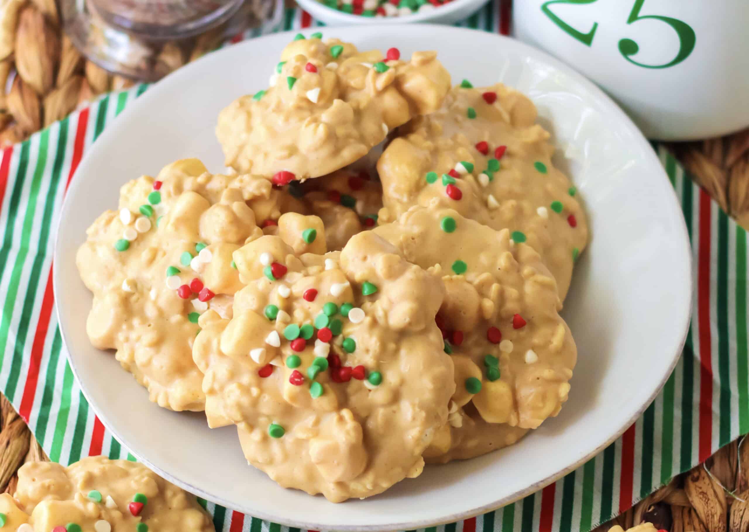 A plate of white chocolate clusters with red, green, and white sprinkles on a striped red, green, and white cloth.