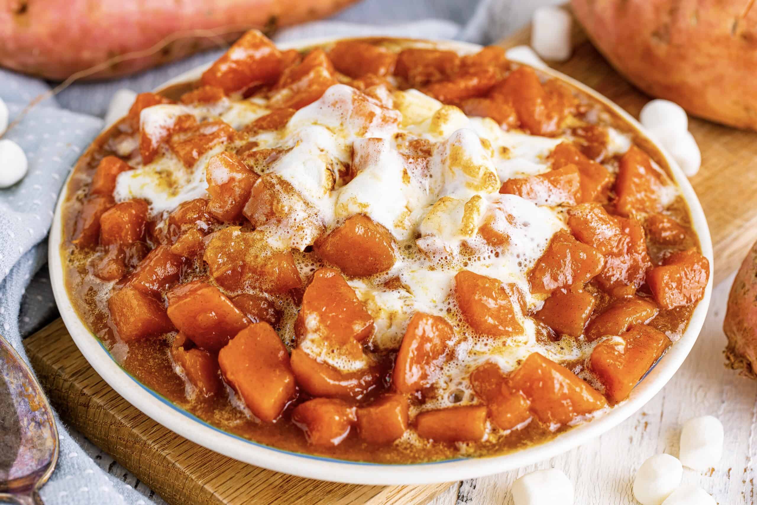 A bowl of sweet potato casserole topped with melted marshmallows, with sweet potatoes and mini marshmallows nearby.