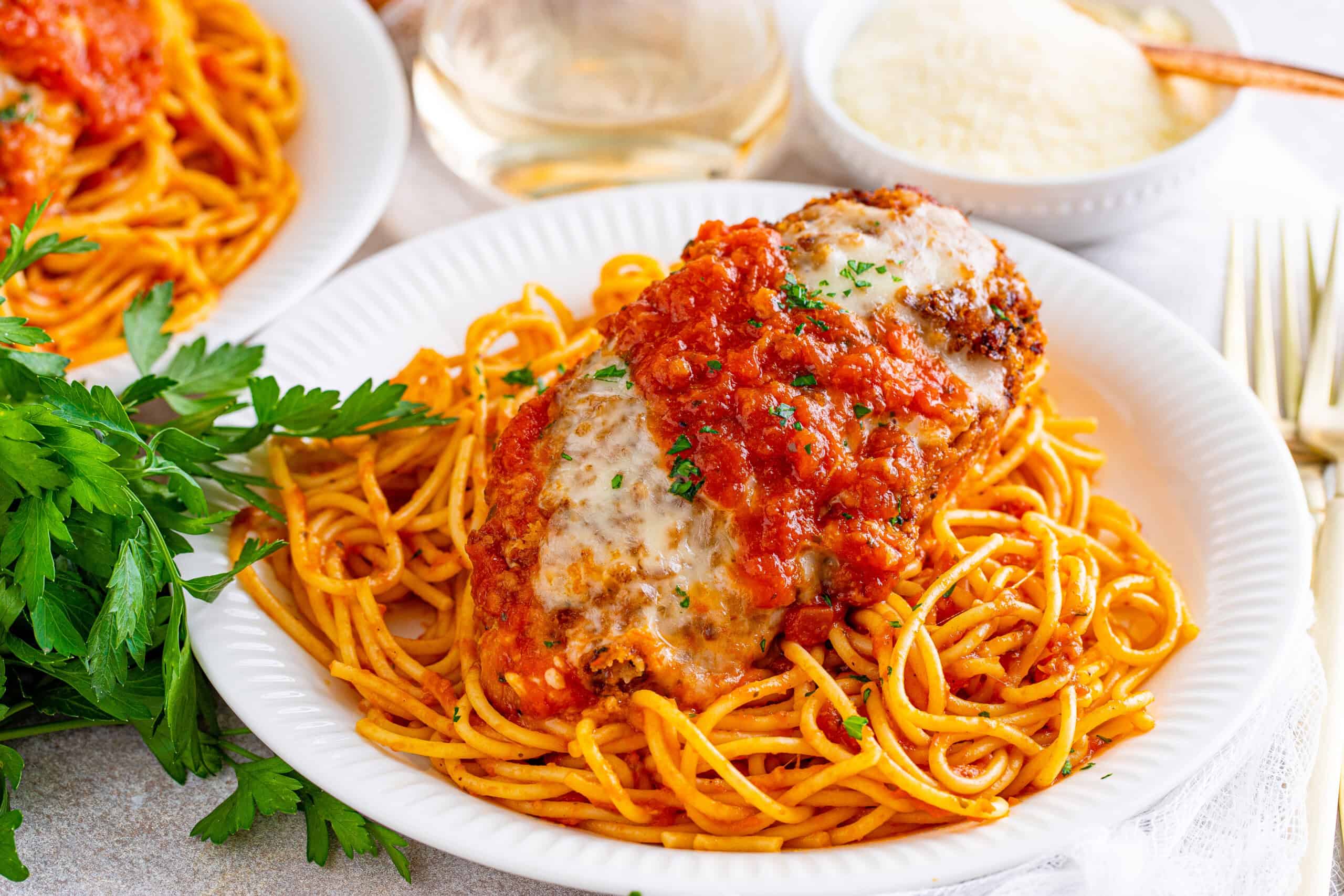 A plate of spaghetti topped with a breaded chicken cutlet, melted cheese, tomato sauce, and parsley.