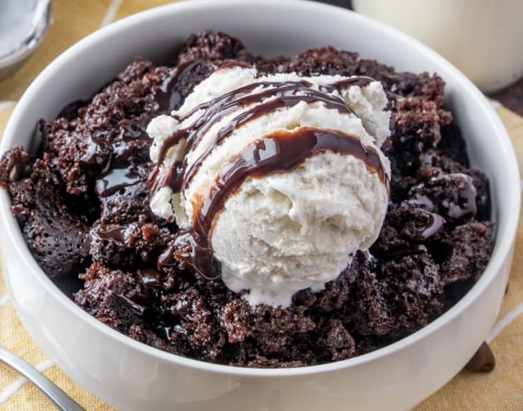 A chocolate lava cake with vanilla ice cream and chocolate syrup on top in a bowl.